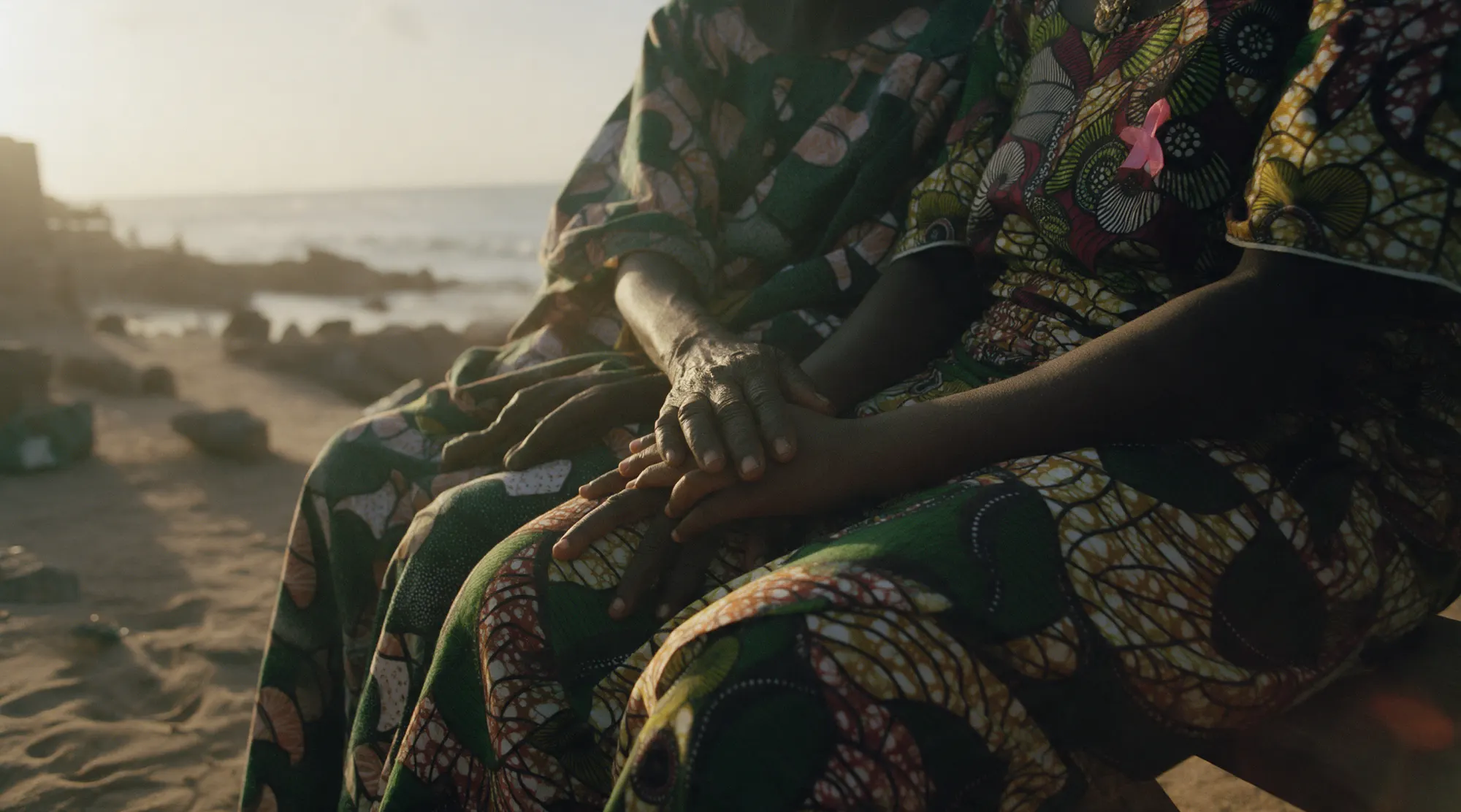 Three generations of women's hands resting on one another, on wax-print cloth.