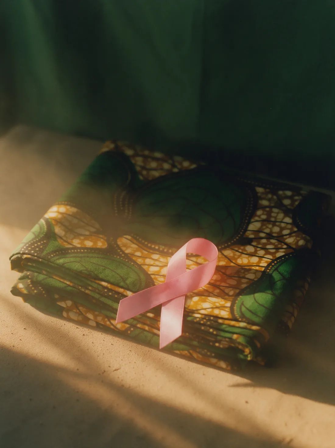 A pink awareness ribbon resting on folded wax-print cloth.